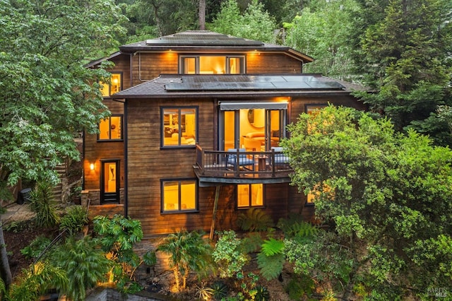 rear view of property featuring a view of trees, a balcony, and solar panels