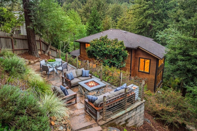 view of patio featuring fence, an outdoor living space with a fire pit, outdoor dining space, and a wooded view