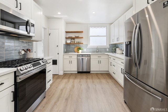 kitchen with light wood-style floors, a sink, appliances with stainless steel finishes, and backsplash