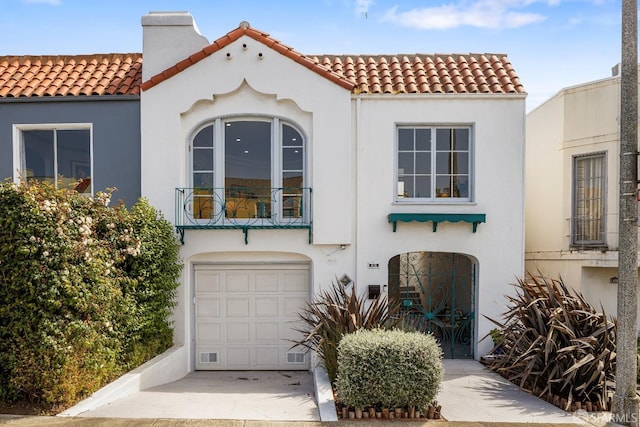 mediterranean / spanish house featuring a chimney, a garage, stucco siding, and a tile roof