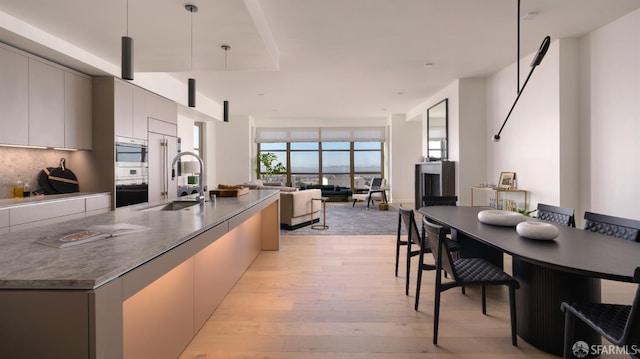 kitchen featuring light wood-style flooring, modern cabinets, a sink, decorative light fixtures, and backsplash