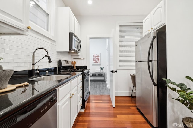 kitchen with appliances with stainless steel finishes, white cabinetry, a sink, and wood finished floors