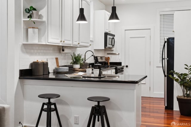 kitchen featuring dark wood finished floors, dark countertops, a breakfast bar area, stainless steel appliances, and white cabinetry