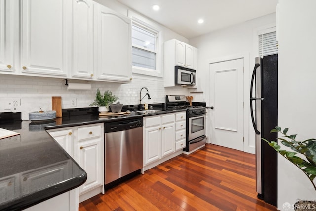 kitchen featuring dark wood finished floors, dark countertops, stainless steel appliances, white cabinetry, and backsplash