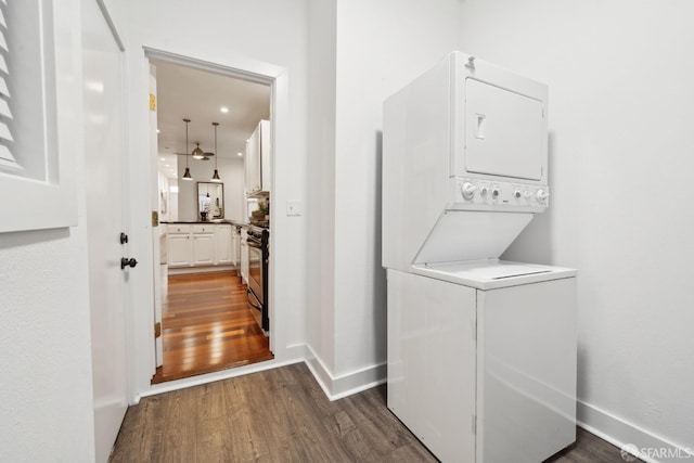 laundry room with dark wood-type flooring, stacked washer / dryer, laundry area, and baseboards