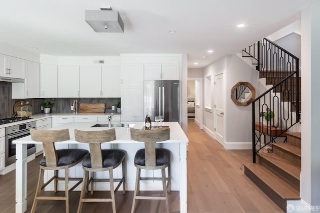 kitchen featuring appliances with stainless steel finishes, light hardwood / wood-style floors, white cabinetry, backsplash, and sink