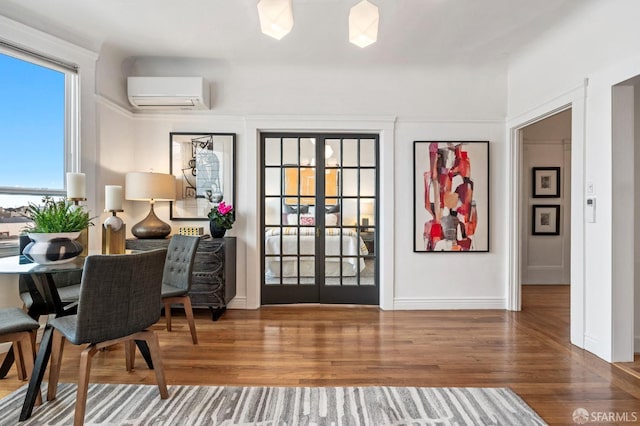 interior space with french doors, a wall mounted air conditioner, wood finished floors, and baseboards