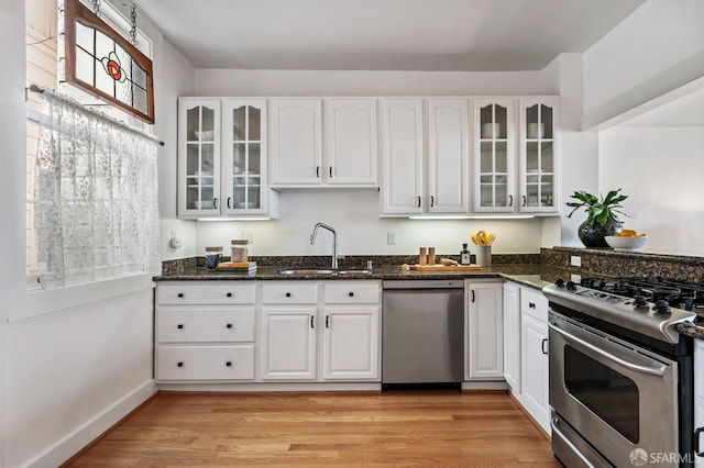 kitchen with stainless steel appliances, light wood-type flooring, a sink, and dark stone countertops