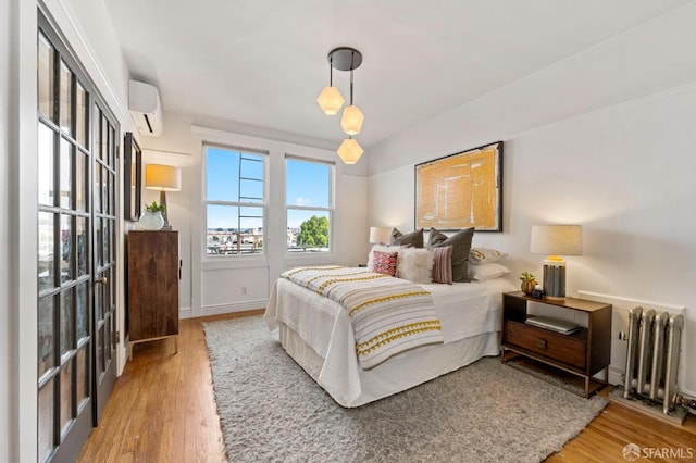 bedroom featuring radiator, baseboards, wood finished floors, and an AC wall unit