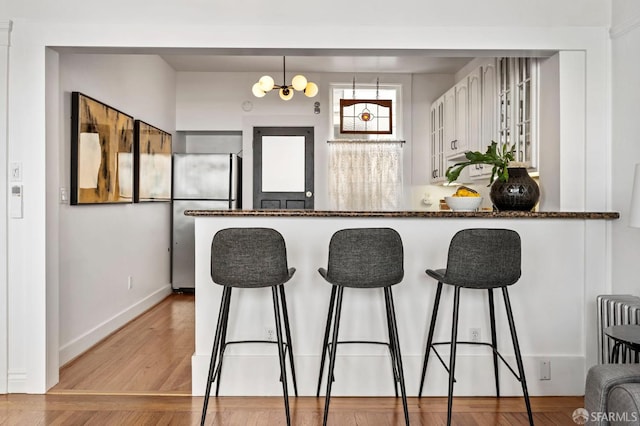 kitchen featuring light wood-style flooring, freestanding refrigerator, a peninsula, a kitchen bar, and white cabinetry