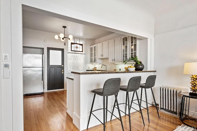 kitchen with radiator, glass insert cabinets, stainless steel refrigerator, a breakfast bar area, and light wood-type flooring