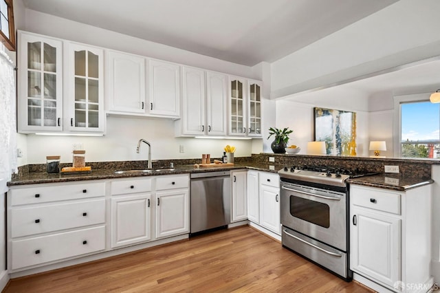 kitchen with white cabinets, appliances with stainless steel finishes, a peninsula, light wood-type flooring, and a sink