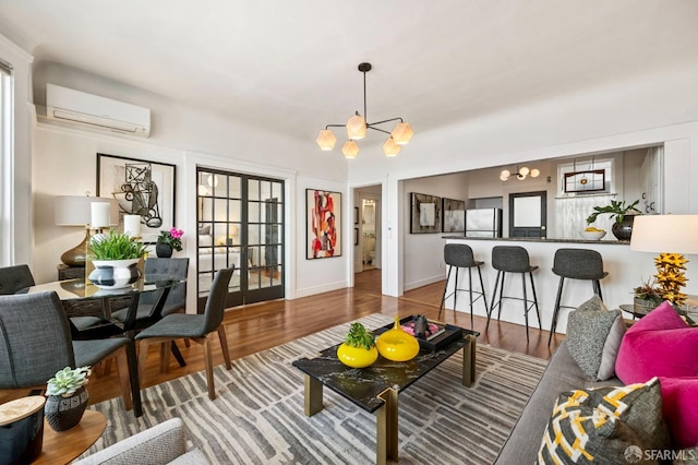 living area featuring french doors, an inviting chandelier, an AC wall unit, wood finished floors, and baseboards