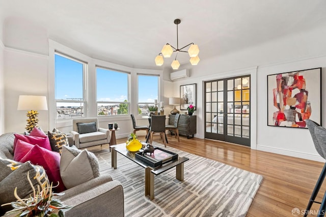 living area featuring an inviting chandelier, baseboards, wood finished floors, and an AC wall unit