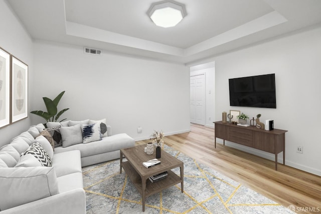 living room with light wood finished floors, baseboards, and a tray ceiling