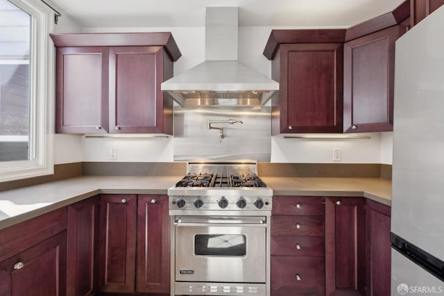 kitchen with wall chimney range hood, dark brown cabinets, plenty of natural light, and stainless steel appliances