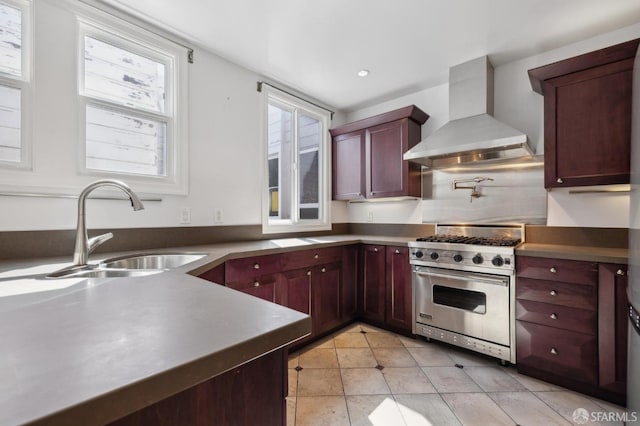 kitchen with luxury range, reddish brown cabinets, wall chimney exhaust hood, and a sink