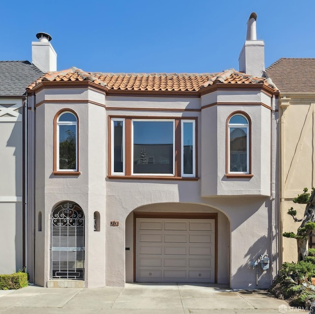 view of front of property with stucco siding, a chimney, an attached garage, and a tiled roof