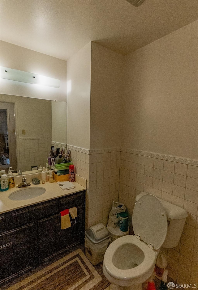 half bath with vanity, tile walls, toilet, and a wainscoted wall