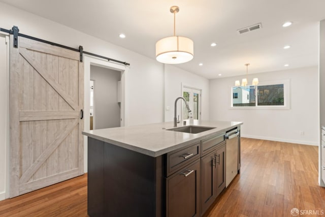 kitchen with a sink, light wood-style flooring, stainless steel dishwasher, and a barn door