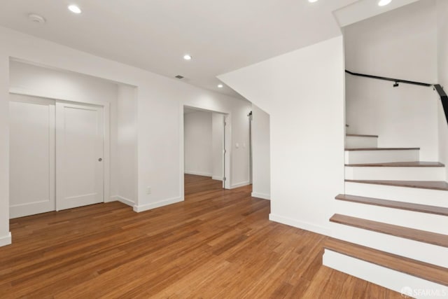 basement featuring light wood-type flooring, baseboards, recessed lighting, and stairs