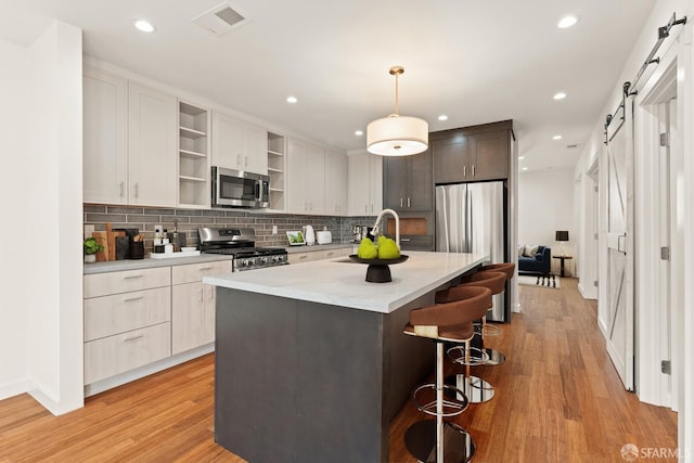 kitchen featuring open shelves, a barn door, appliances with stainless steel finishes, light wood-style floors, and a sink