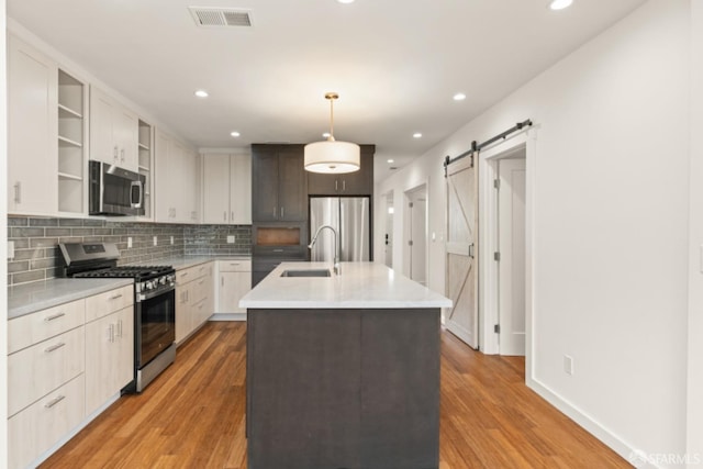 kitchen with a barn door, visible vents, stainless steel appliances, open shelves, and a sink