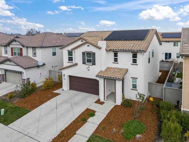 view of front of house featuring a tile roof, solar panels, concrete driveway, fence, and a garage