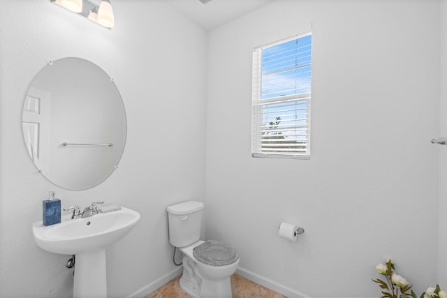 half bath featuring baseboards, a sink, and toilet
