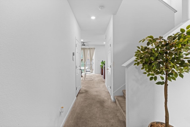 hall with baseboards, stairs, and light colored carpet