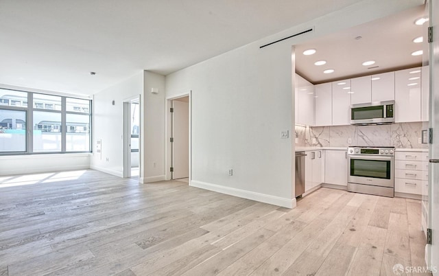 kitchen with backsplash, white cabinets, light hardwood / wood-style floors, and appliances with stainless steel finishes