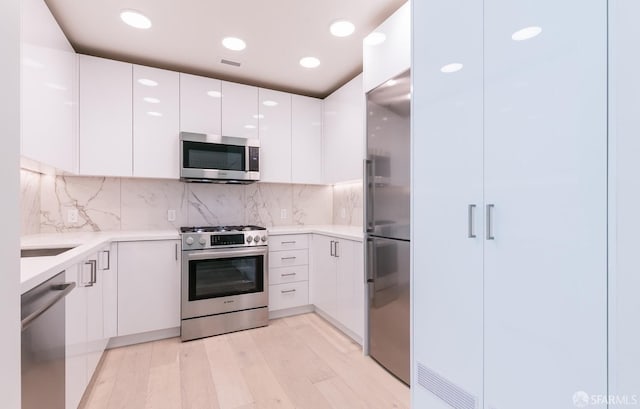 kitchen featuring white cabinets, light wood-type flooring, tasteful backsplash, and high end appliances