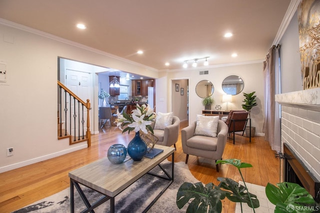 living area featuring stairway, wood finished floors, visible vents, crown molding, and a brick fireplace