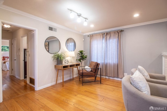 sitting room featuring baseboards, visible vents, light wood finished floors, and ornamental molding