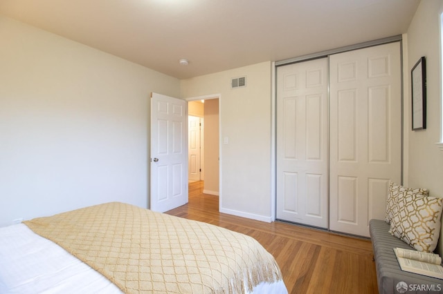 bedroom featuring wood finished floors, visible vents, a closet, and baseboards