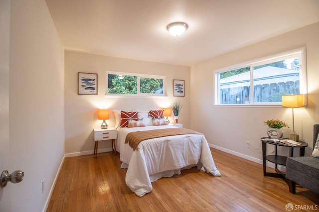 bedroom with baseboards, multiple windows, and light wood finished floors