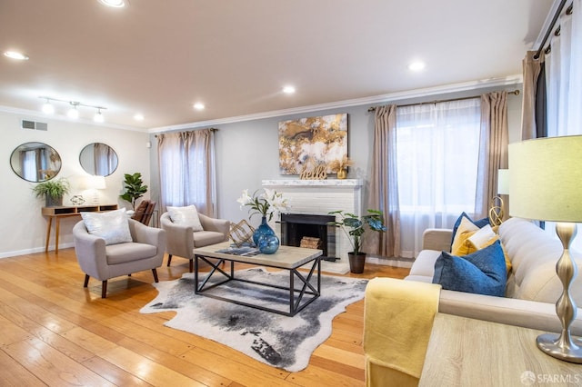 living room featuring baseboards, visible vents, a fireplace, ornamental molding, and light wood-type flooring