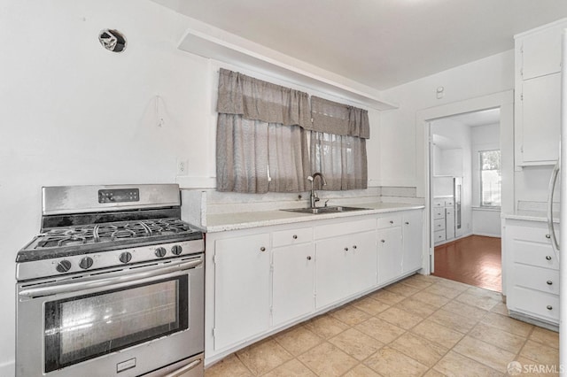 kitchen featuring white cabinets, light countertops, a sink, and stainless steel range with gas cooktop