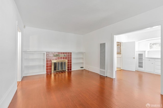 unfurnished living room featuring a tiled fireplace, baseboards, and wood finished floors