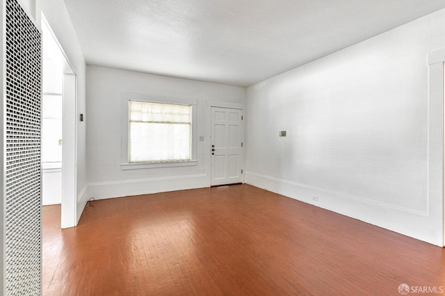 unfurnished room with baseboards, a heating unit, and wood finished floors