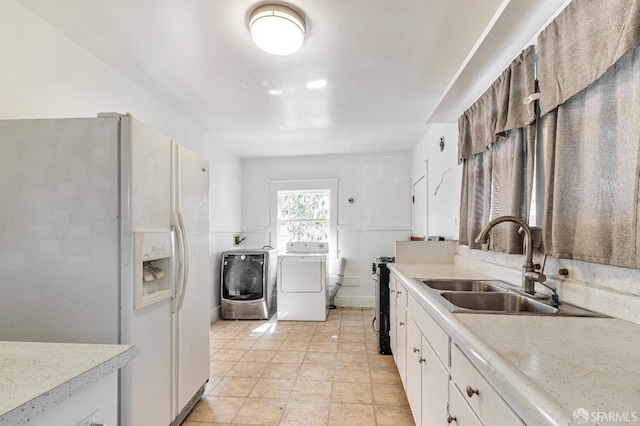 kitchen featuring white cabinets, white fridge with ice dispenser, a sink, light countertops, and washer and clothes dryer