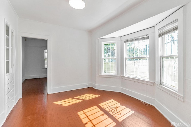 unfurnished room featuring plenty of natural light, wood-type flooring, and baseboards