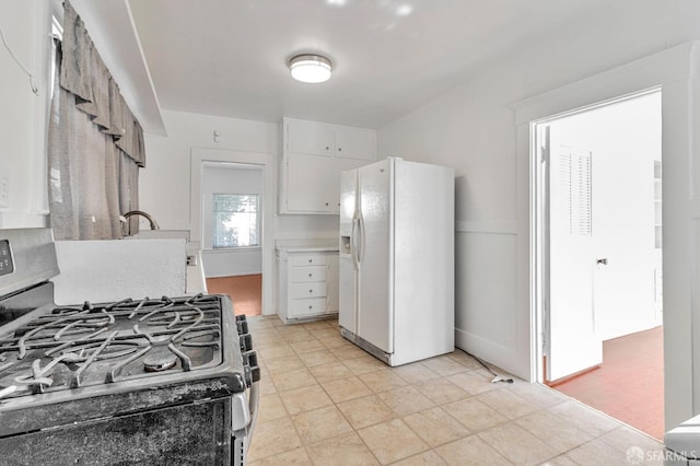 kitchen with white refrigerator with ice dispenser, stainless steel range with gas stovetop, light countertops, and white cabinetry