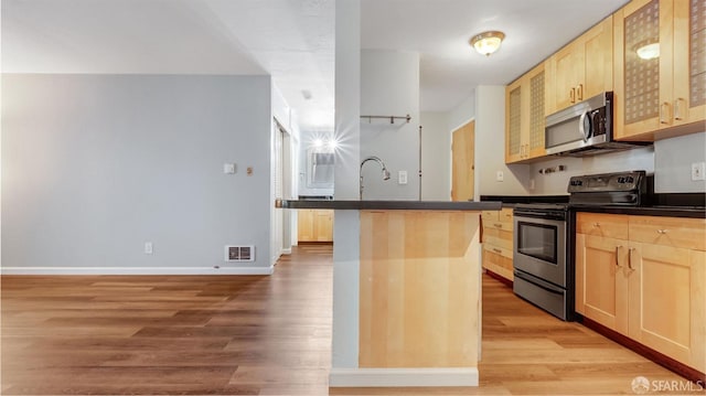 kitchen with light brown cabinetry, a kitchen bar, a kitchen island with sink, light hardwood / wood-style floors, and stainless steel appliances