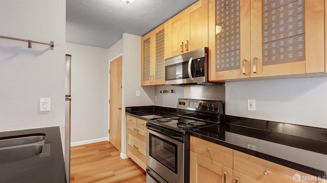 kitchen with stainless steel appliances, light brown cabinetry, sink, and light wood-type flooring