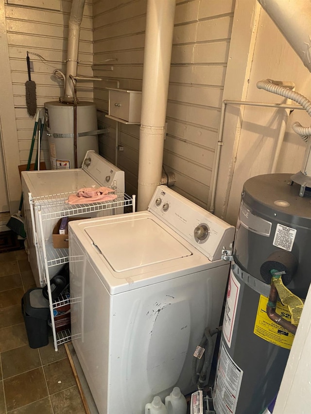 washroom with gas water heater, washer / dryer, wood walls, and dark tile patterned floors