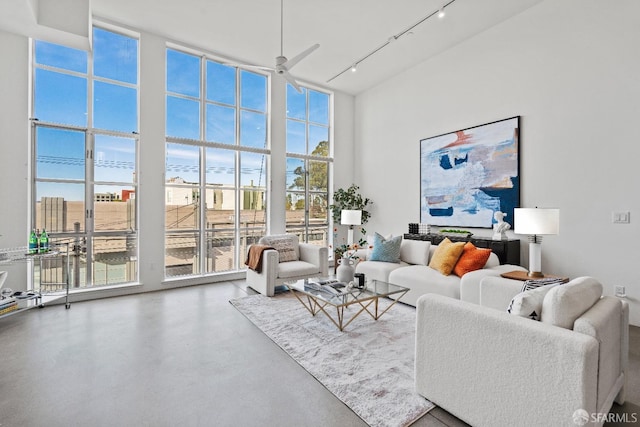 living room featuring a towering ceiling, ceiling fan, a wall of windows, concrete floors, and track lighting