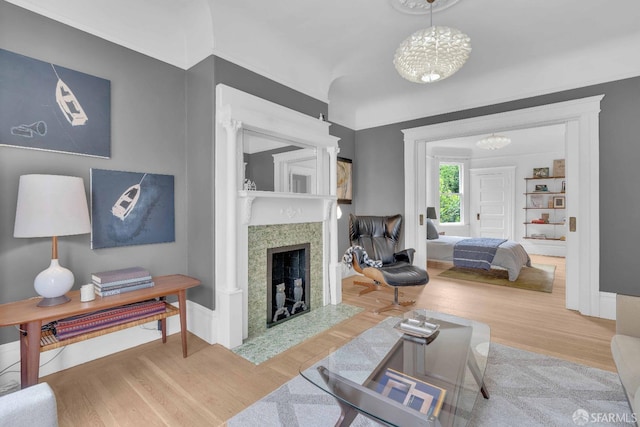 living room with baseboards, an inviting chandelier, a fireplace with flush hearth, and wood finished floors