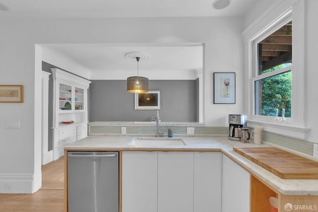 kitchen with stainless steel dishwasher, hanging light fixtures, a sink, decorative backsplash, and white cabinets