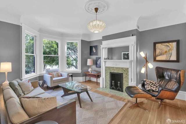 living room with wood finished floors, baseboards, a fireplace with flush hearth, and a notable chandelier